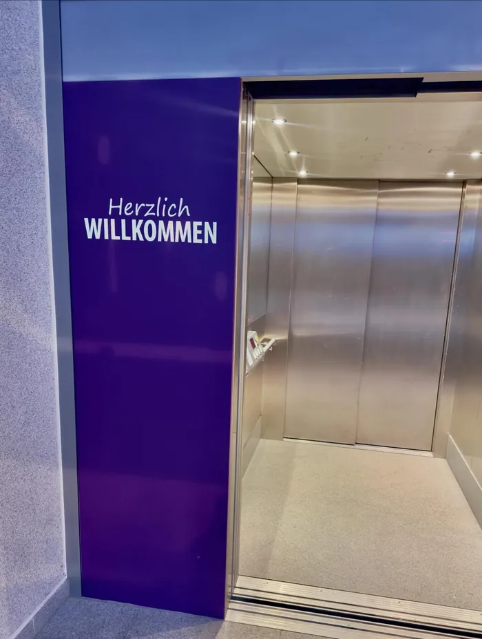 Aufzug im Gebäude mit lila Wand und Schriftzug „Herzlich Willkommen“